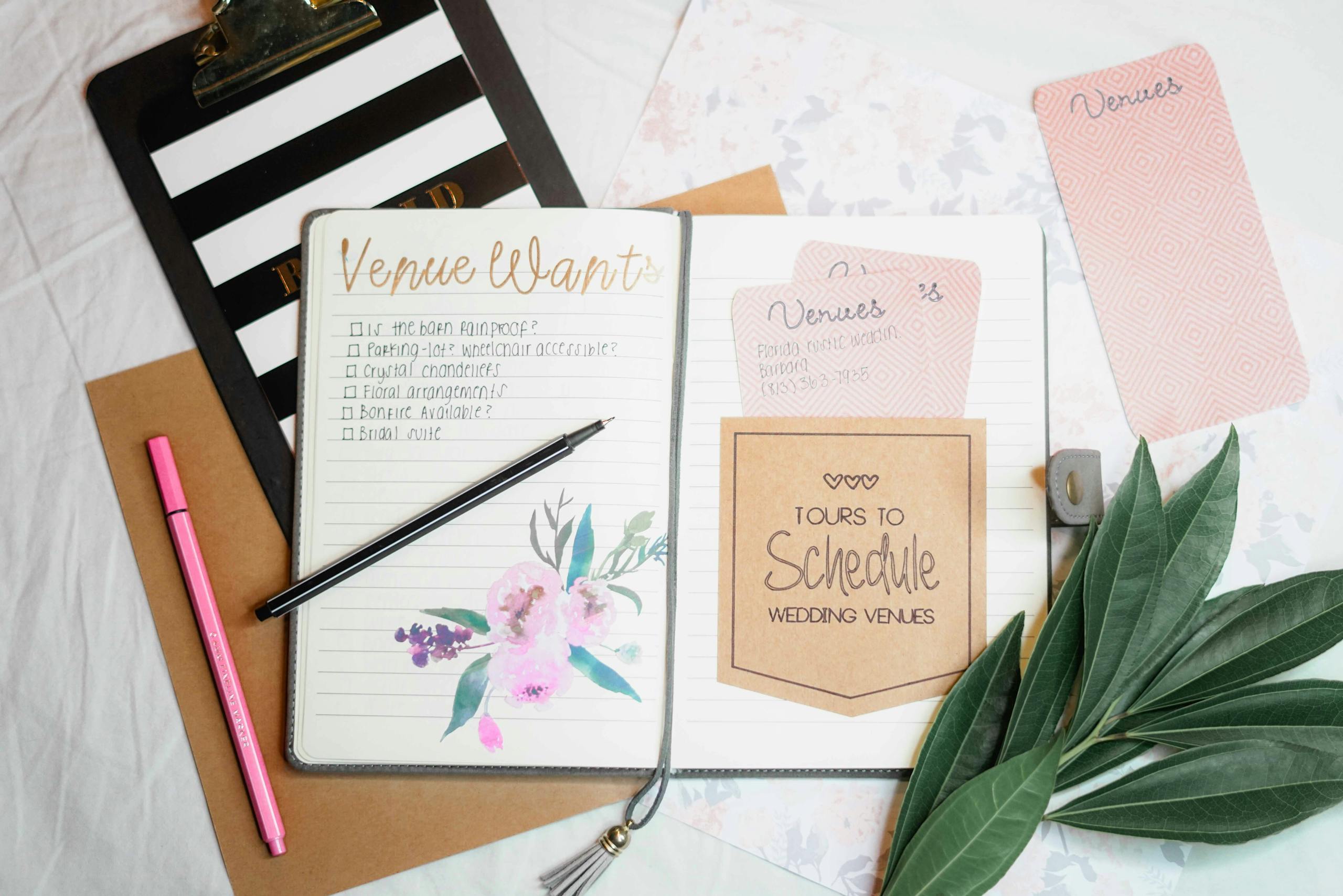 Flat lay of wedding planning materials including a journal, leaves, and stationery.